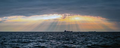 Ships on the horizon with sunlight showing through clouds